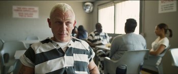 Movie still from “Logan Lucky” (2017), directed by Steven Soderbergh – A man in prison garb standing in front of a group of people; Medium shot, Over the shoulder angle
