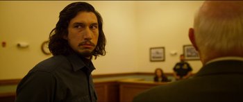 Movie still from “Logan Lucky” (2017), directed by Steven Soderbergh – A man with long black hair in a courtroom; Medium shot, Over the shoulder angle