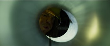 Movie still from “Logan Lucky” (2017), directed by Steven Soderbergh – A man wearing a hard hat looking through a hole in the wall; Extreme Close Up shot, Low angle