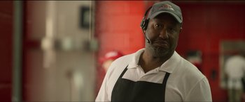 Movie still from “Logan Lucky” (2017), directed by Steven Soderbergh – A man wearing an apron and a baseball cap; Close Up shot, Over the shoulder angle