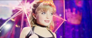 Movie still from “Logan Lucky” (2017), directed by Steven Soderbergh – A young woman holding an umbrella in front of a purple background; Close Up shot, High angle