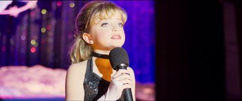 Movie still from “Logan Lucky” (2017), directed by Steven Soderbergh – A young girl holding a microphone up to her face; Close Up shot, High angle