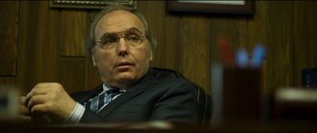 Movie still from “Logan Lucky” (2017), directed by Steven Soderbergh – An older man in a suit and glasses; Close Up shot, Over the shoulder angle