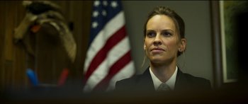 Movie still from “Logan Lucky” (2017), directed by Steven Soderbergh – A woman wearing a suit and tie in front of an american flag; Close Up shot, Low angle