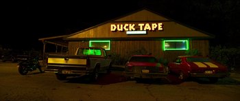 Movie still from “Logan Lucky” (2017), directed by Steven Soderbergh – Two trucks parked in front of a duck tape store; Wide shot, Low angle