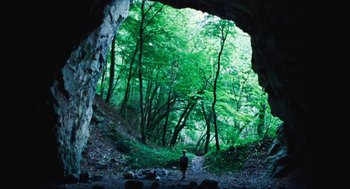 Movie still from “Lore” (2012), directed by Cate Shortland – A person standing in front of an opening in a cave; Extreme Wide shot, High angle