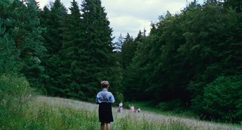 Movie still from “Lore” (2012), directed by Cate Shortland – A woman standing in the middle of a field with trees in the background; Extreme Wide shot, High angle