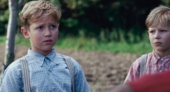Movie still from “Lore” (2012), directed by Cate Shortland – A young boy in a plaid shirt is standing in a field; Close Up shot, Over the shoulder angle