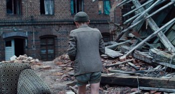 Movie still from “Lore” (2012), directed by Cate Shortland – A man in a hat and shorts standing in rubble; Medium shot, High angle