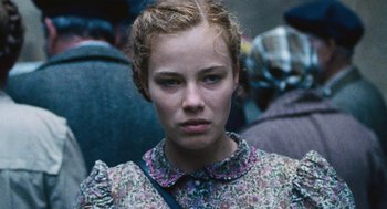 Movie still from “Lore” (2012), directed by Cate Shortland – A young woman in a floral dress is looking at the camera; Close Up shot, Low angle