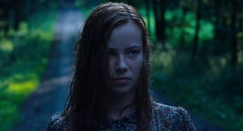 Movie still from “Lore” (2012), directed by Cate Shortland – A young woman with long hair is standing in the woods; Close Up shot, Over the shoulder angle