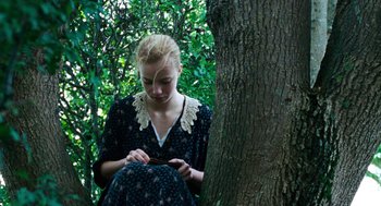 Movie still from “Lore” (2012), directed by Cate Shortland – A woman sitting on a tree in the woods; Medium shot, High angle