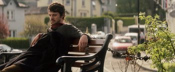Movie still from “Leap Year” (2010), directed by Anand Tucker – A man sitting on top of a wooden park bench; Medium shot, Low angle