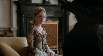 Movie still from “Love & Friendship” (2016), directed by Whit Stillman – A woman dressed in period clothing sitting in front of a fireplace; Medium shot, Over the shoulder angle