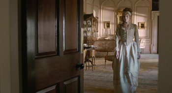 Movie still from “Love & Friendship” (2016), directed by Whit Stillman – A woman dressed in period clothing standing in front of an open door; Wide shot, Over the shoulder angle