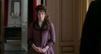 Movie still from “Love & Friendship” (2016), directed by Whit Stillman – A woman in a purple dress standing next to a door; Medium shot, Over the shoulder angle