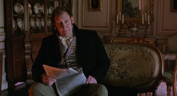 Movie still from “Love & Friendship” (2016), directed by Whit Stillman – A man sitting on a couch while holding a newspaper; Medium shot, Over the shoulder angle