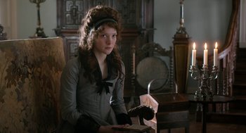 Movie still from “Love & Friendship” (2016), directed by Whit Stillman – A young woman in a gray dress and a black hat; Medium shot, Over the shoulder angle