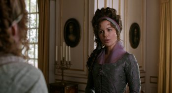 Movie still from “Love & Friendship” (2016), directed by Whit Stillman – A woman in a gray dress standing next to a window; Medium shot, Over the shoulder angle