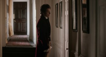 Movie still from “Love & Friendship” (2016), directed by Whit Stillman – A man standing in front of an open door in a room; Medium shot, Over the shoulder angle