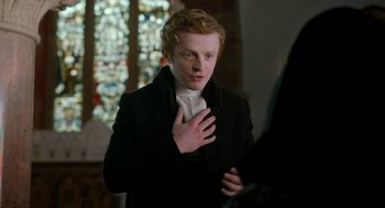 Movie still from “Love & Friendship” (2016), directed by Whit Stillman – A man in a black coat is standing in front of a stained glass window; Close Up shot, Over the shoulder angle