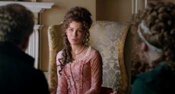 Movie still from “Love & Friendship” (2016), directed by Whit Stillman – A woman in a pink dress sitting in a chair; Close Up shot, Over the shoulder angle