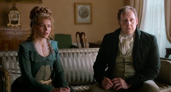 Movie still from “Love & Friendship” (2016), directed by Whit Stillman – A man and a woman sitting on a couch in a living room; Medium shot, Over the shoulder angle