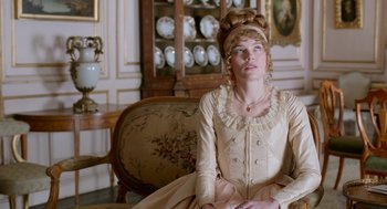 Movie still from “Love & Friendship” (2016), directed by Whit Stillman – A woman sitting on a chair in a room; Medium shot, Over the shoulder angle