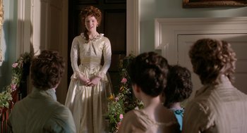 Movie still from “Love & Friendship” (2016), directed by Whit Stillman – A woman standing in front of a group of people; Medium shot, Over the shoulder angle