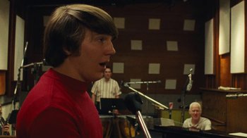 Movie still from “Love & Mercy” (2014), directed by Bill Pohlad – A man in a red shirt talking into a microphone in front of other men; Close Up shot, Low angle