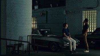 Movie still from “Love & Mercy” (2014), directed by Bill Pohlad – A man sitting on the back of a car in a garage; Wide shot, High angle