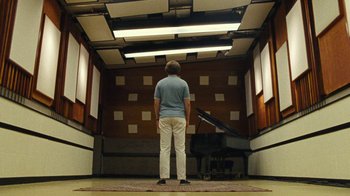 Movie still from “Love & Mercy” (2014), directed by Bill Pohlad – A man standing in front of a piano in a room; Wide shot, Low angle