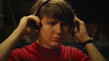 Movie still from “Love & Mercy” (2014), directed by Bill Pohlad – A young man wearing a pair of headphones and a red t - shirt; Close Up shot, Low angle
