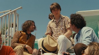 Movie still from “Love & Mercy” (2014), directed by Bill Pohlad – A group of people sitting on the ground in front of a body of water; Medium shot, Over the shoulder angle