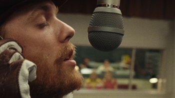 Movie still from “Love & Mercy” (2014), directed by Bill Pohlad – A man with a red beard is singing into a microphone; Extreme Close Up shot, Over the shoulder angle