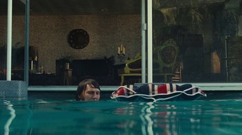 Movie still from “Love & Mercy” (2014), directed by Bill Pohlad – A woman swimming in a swimming pool with a dog in the water; Wide shot, High angle