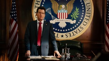 Movie still from “Machete Kills” (2013), directed by Robert Rodriguez – A man standing in front of a desk in front of an american eagle logo; Medium shot, Low angle