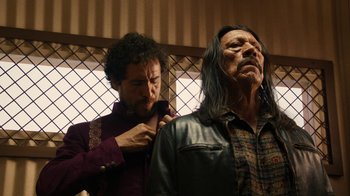 Movie still from “Machete Kills” (2013), directed by Robert Rodriguez – A man with long black hair is standing next to another man with long black hair; Medium shot, Low angle