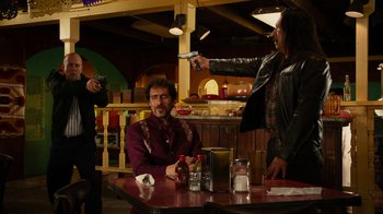 Movie still from “Machete Kills” (2013), directed by Robert Rodriguez – A group of people sitting at a table with a gun; Medium shot, Over the shoulder angle