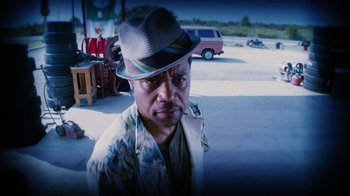 Movie still from “Machete Kills” (2013), directed by Robert Rodriguez – A man with a hat on and a car in the background; Close Up shot, Over the shoulder angle