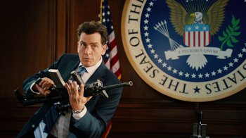 Movie still from “Machete Kills” (2013), directed by Robert Rodriguez – A man in a suit and tie holding a gun in front of an american flag; Medium shot, High angle