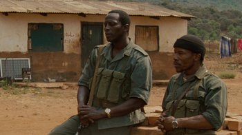 Movie still from “Machine Gun Preacher” (2011), directed by Marc Forster – Two men sitting next to each other in front of a building; Medium shot, Over the shoulder angle