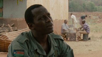 Movie still from “Machine Gun Preacher” (2011), directed by Marc Forster – A man sitting on the ground in front of a building; Close Up shot, Over the shoulder angle