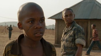 Movie still from “Machine Gun Preacher” (2011), directed by Marc Forster – A young man with a shaved head and a man with a shaved head standing in front of a building; Close Up shot, Over the shoulder angle