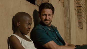 Movie still from “Machine Gun Preacher” (2011), directed by Marc Forster – A man standing next to another man in front of a brick wall; Close Up shot, Over the shoulder angle