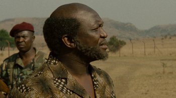 Movie still from “Machine Gun Preacher” (2011), directed by Marc Forster – An older man with a bald head is looking off into the distance; Close Up shot, Over the shoulder angle