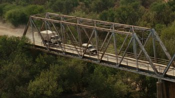 Movie still from “Machine Gun Preacher” (2011), directed by Marc Forster – A truck is driving across a bridge over a river; Extreme Wide shot, Overhead angle