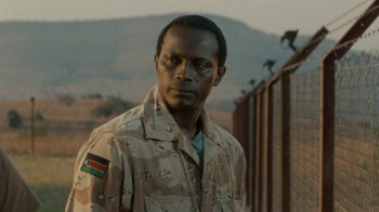 Movie still from “Machine Gun Preacher” (2011), directed by Marc Forster – A man in a military uniform standing in front of a fence; Close Up shot, Over the shoulder angle