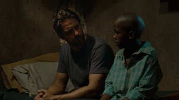 Movie still from “Machine Gun Preacher” (2011), directed by Marc Forster – A man sitting next to a young boy in front of a window; Medium shot, Over the shoulder angle