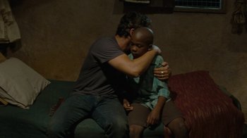 Movie still from “Machine Gun Preacher” (2011), directed by Marc Forster – A man sitting on a couch hugging a young man; Medium shot, Over the shoulder angle